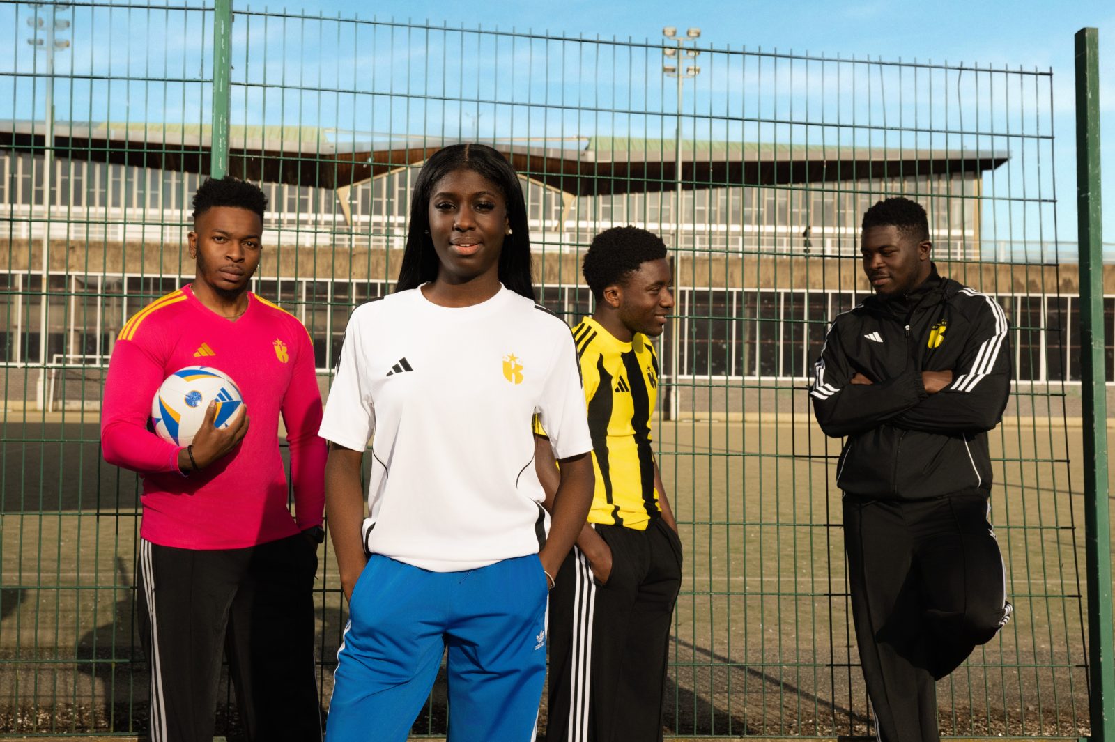 Four young athletes in football kit standing on an outdoor multi-sport court