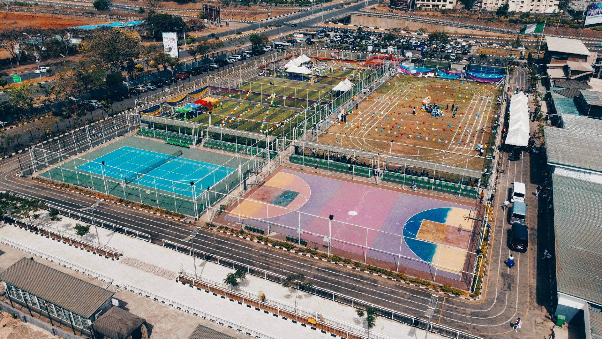 Aerial view of a multi-sport activity complex — football pitches, tennis and basketball courts, a running track and event marquees